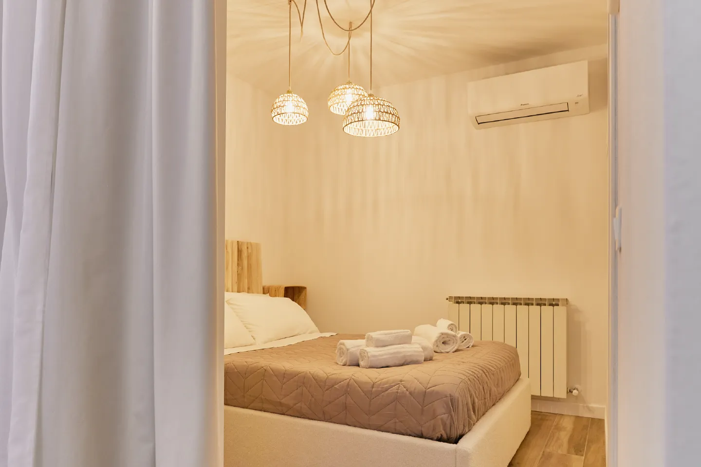 Camera da letto dell'Appartamento Cinzio a Chioggia con letto matrimoniale, climatizzatore Daikin, termosifone e lampadario moderno a tre sospensioni intrecciate.
