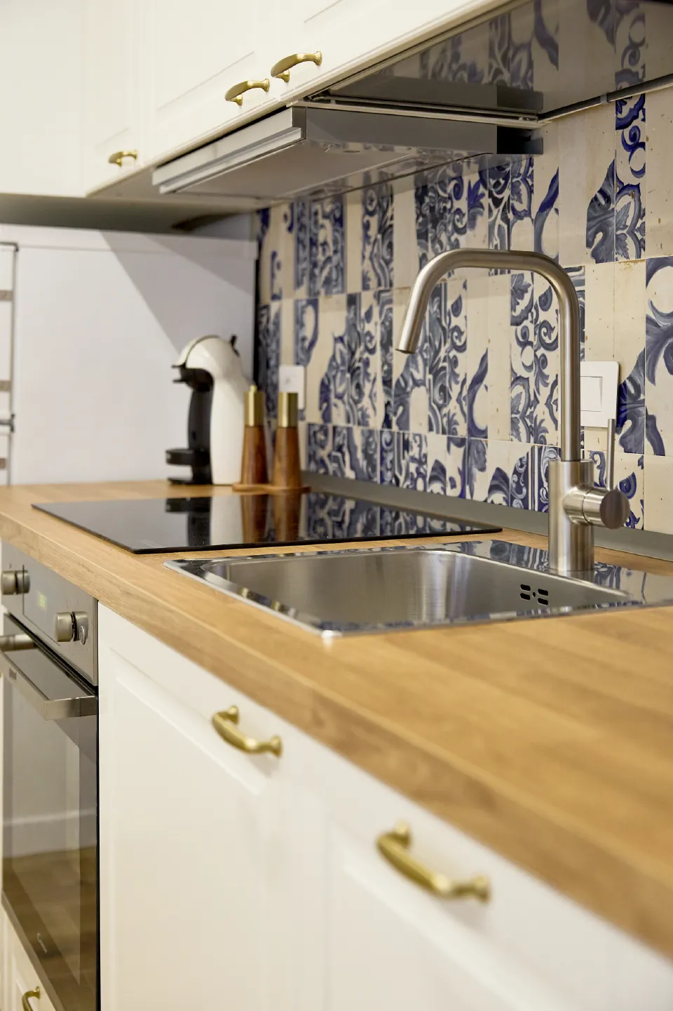 Piano lavoro della cucina in legno con lavello in acciaio, miscelatore moderno, piastra a induzione e macchina del caffè.